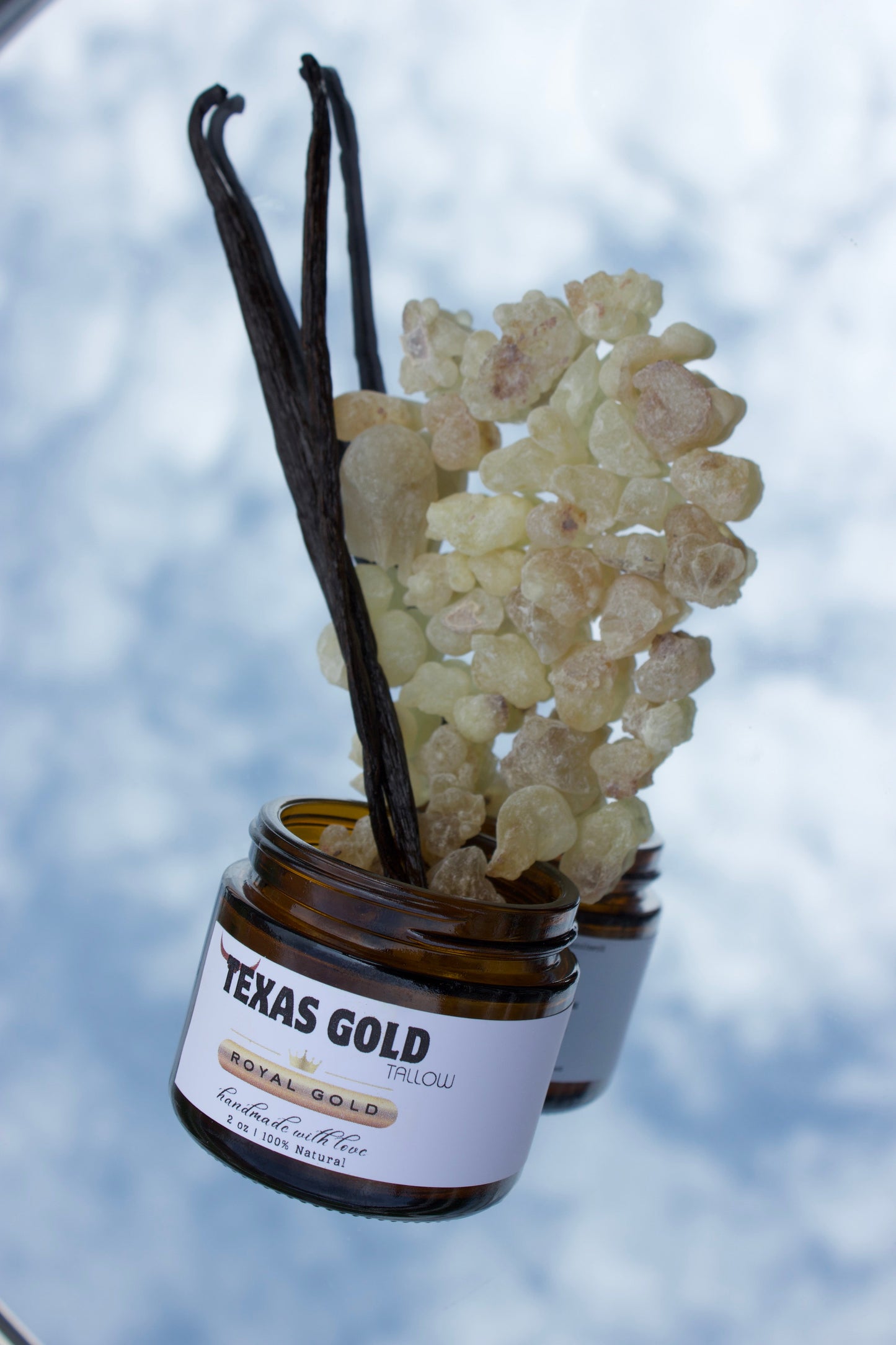 Texas Gold Tallow Royal Gold frankincense, resin and vanilla bean coming out of the jar, showing the real ingredients, with the sky background