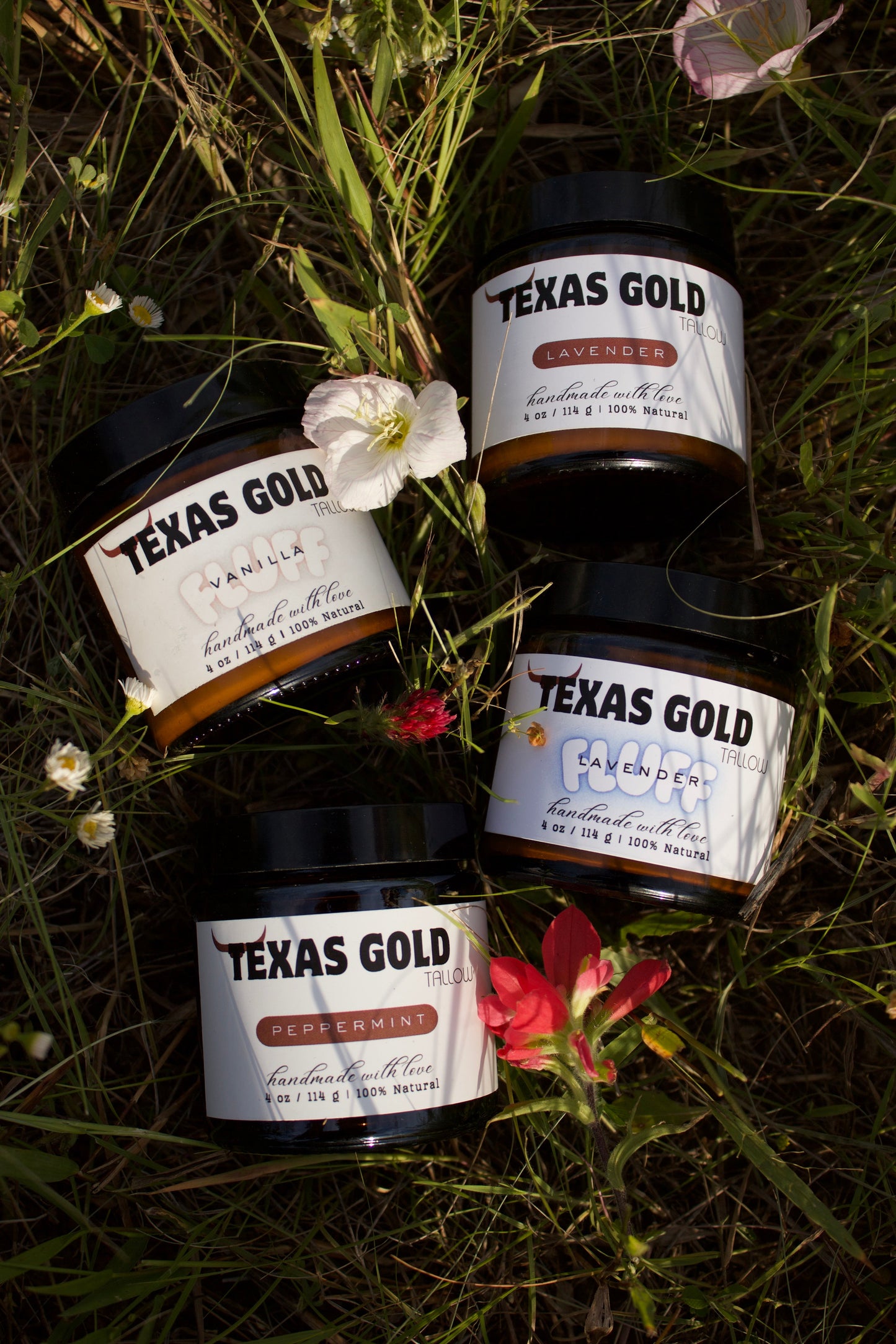 4 Texas Gold Tallow grass fed and grass finished beef tallow balms laying in the grass with flowers