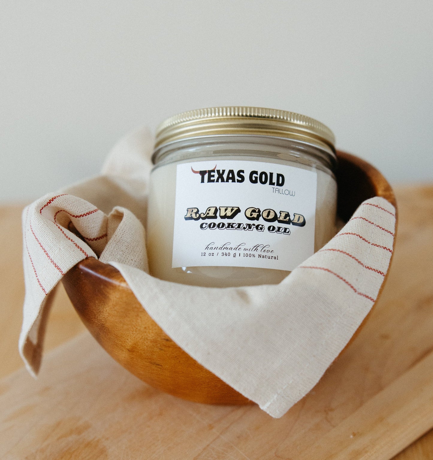 Texas Gold Tallow Raw Gold Cooking Oil in a glass jar grass fed and grass finished inside a bowl on a cutting board