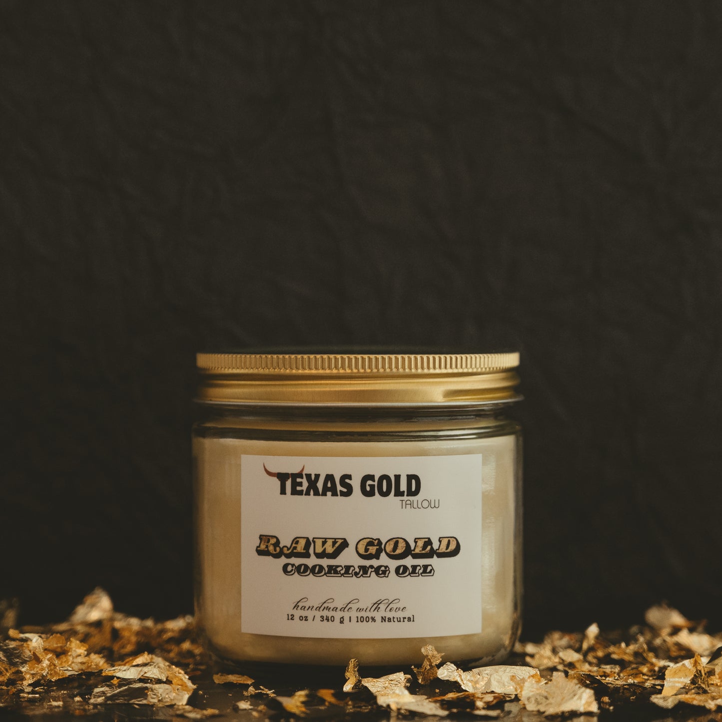 Texas gold tallow raw gold cooking oil in a 12 ounce glass jar with gold lid and a black background with gold flakes
